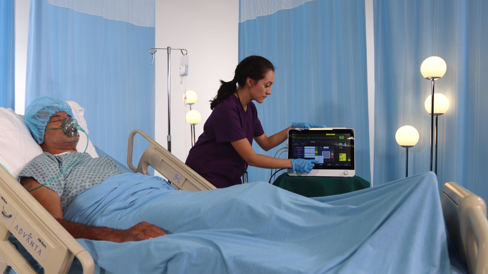 brio-x70-patient-monitor-in-icu-clinical-use Nurse operating a Bionet Brio X70 patient monitor beside an ICU patient receiving oxygen therapy