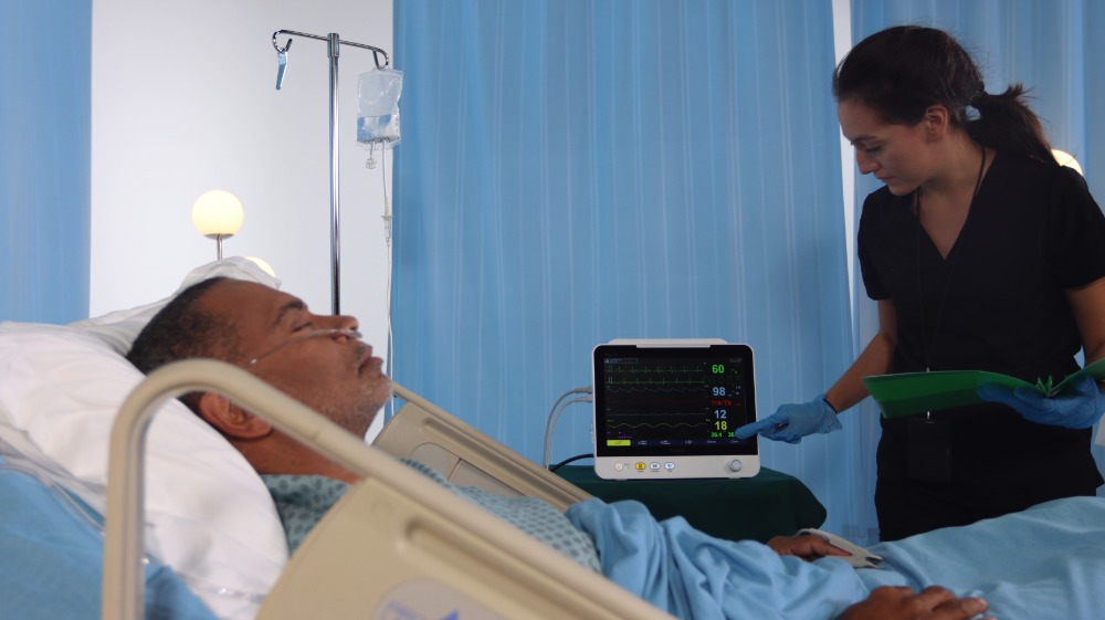 brio-x50-patient-monitor-in-clinical-use Brio X50 patient monitor in clinical use at bedside with a clinician reviewing vital signs of a sedated patient